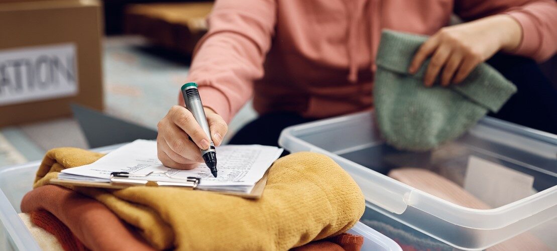 Woman sorting her belongings into different boxes and keeping organized by using a list.