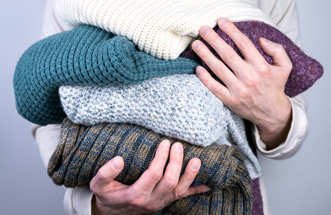 Man holding a pile of sweaters.