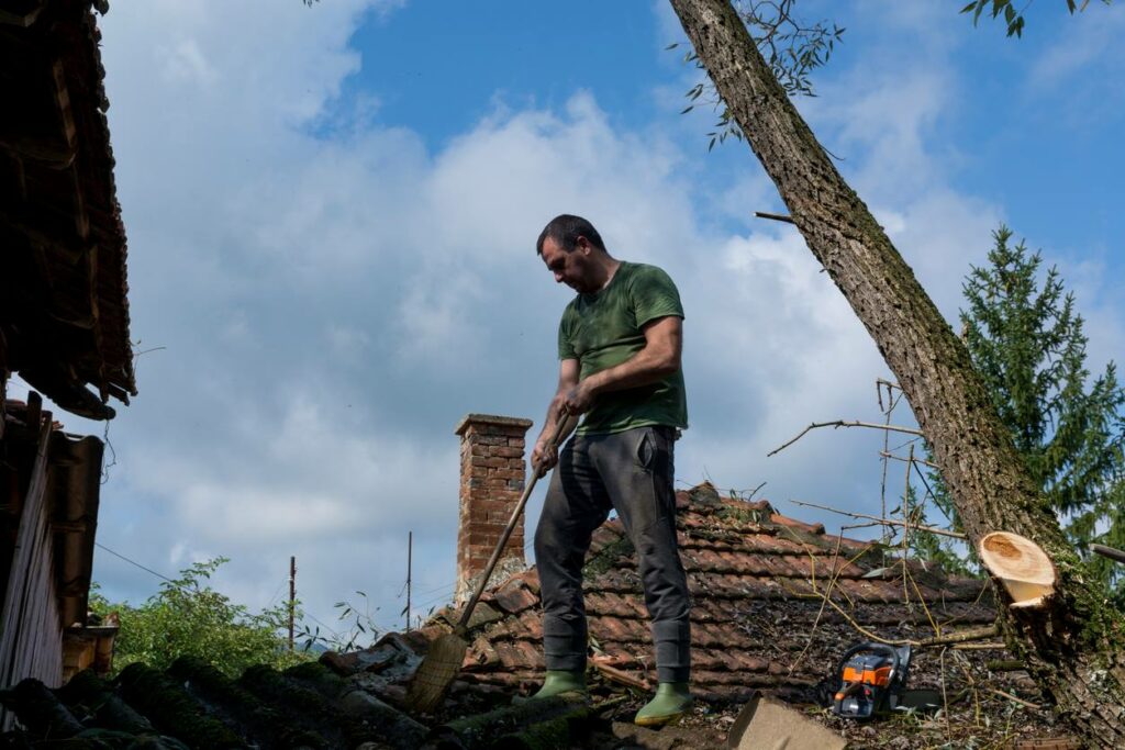 A man on a roof cleaning tiles from leaves and fallen branches.