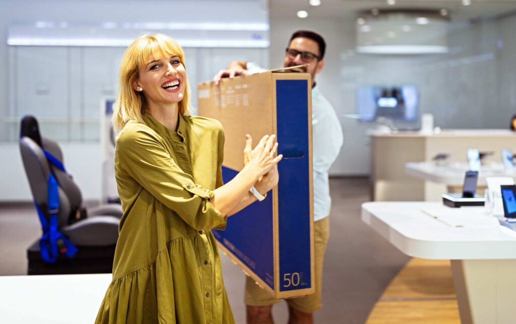 A cheerful couple carrying a television, representing the need for climate-controlled storage for electronics.