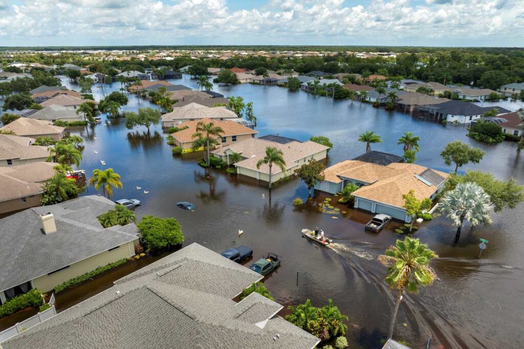 A flooded Florida neighborhood after a hurricane, with submerged streets, homes, and rescue boats navigating water.