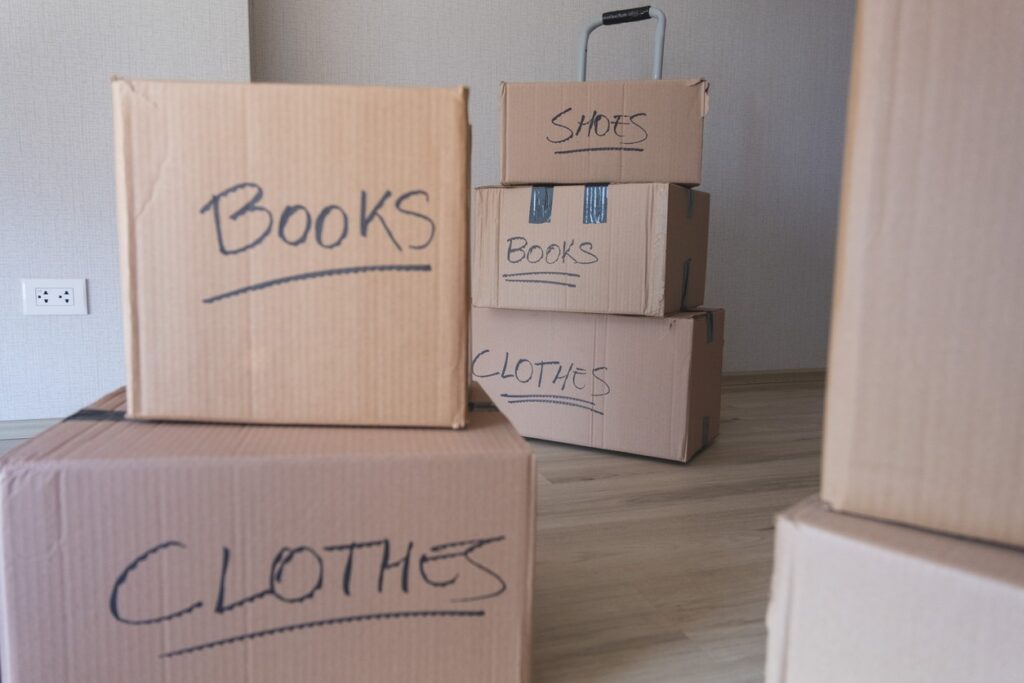 Cardboard moving boxes labeled "books," "clothes," and "shoes" stacked in a room.