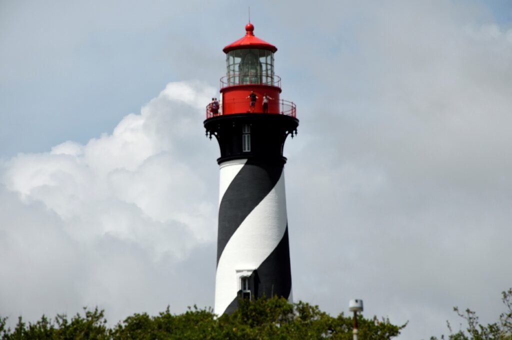 The St. Augustine Lighthouse with black and white spiral stripes and a red top, standing tall against a cloudy sky.